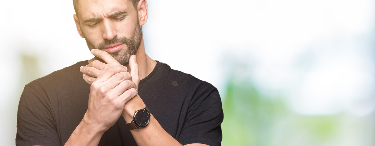 A man with a beard in a black shirt grips his left hand with his right.