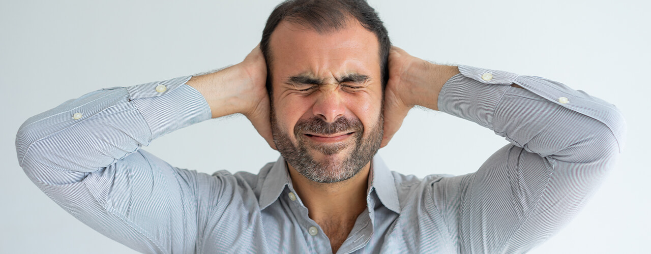 Man covers his ears with his hands and has his eyes closed tight.
