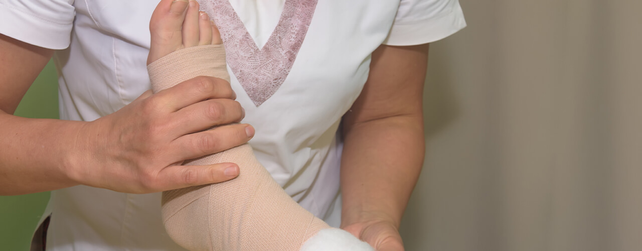 A person has their foot and ankle up in the air, wrapped in a bandage as a therapist helps to hold it up.