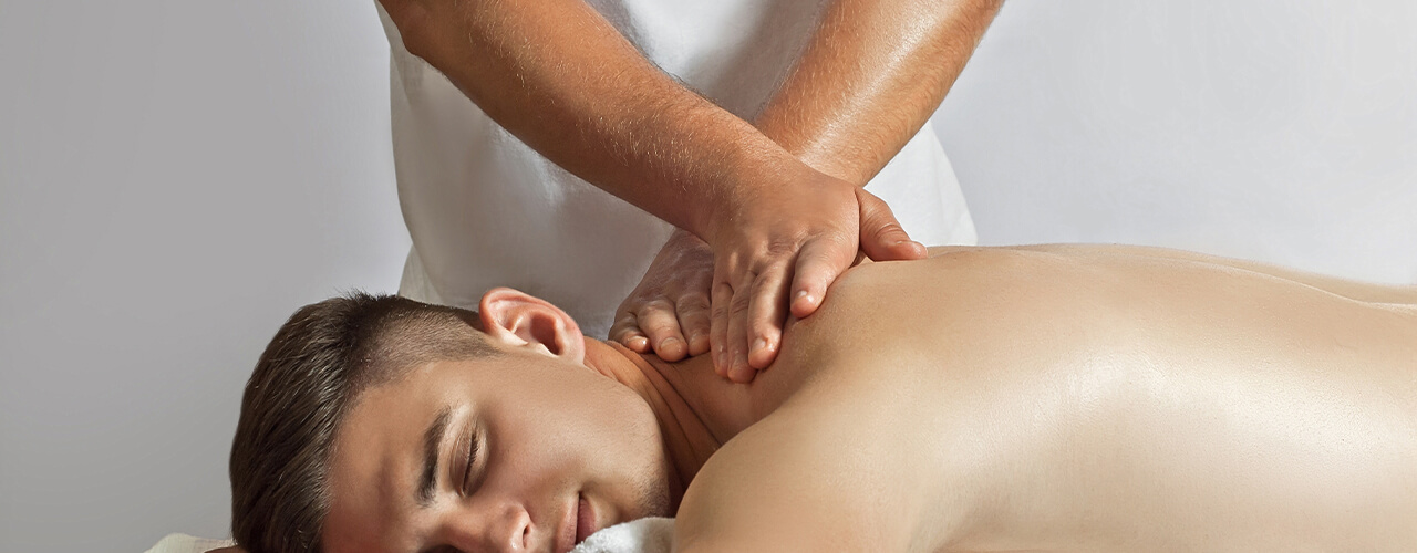 A man lays shirtless stomach down while a therapist performs manual therapy on their upper back.