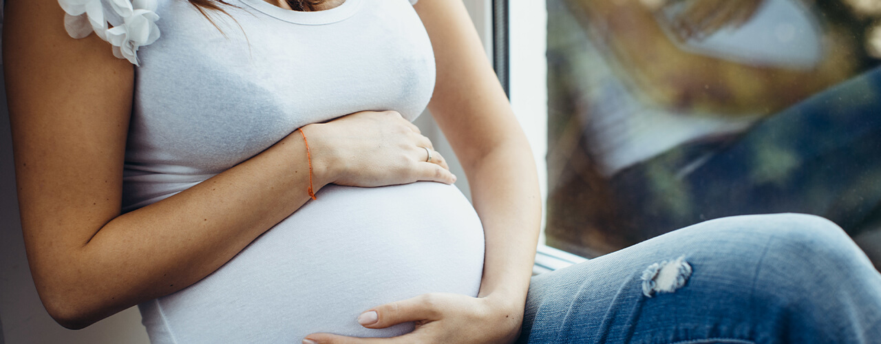 Pregnant woman cradles her stomach with both hands while sitting down.