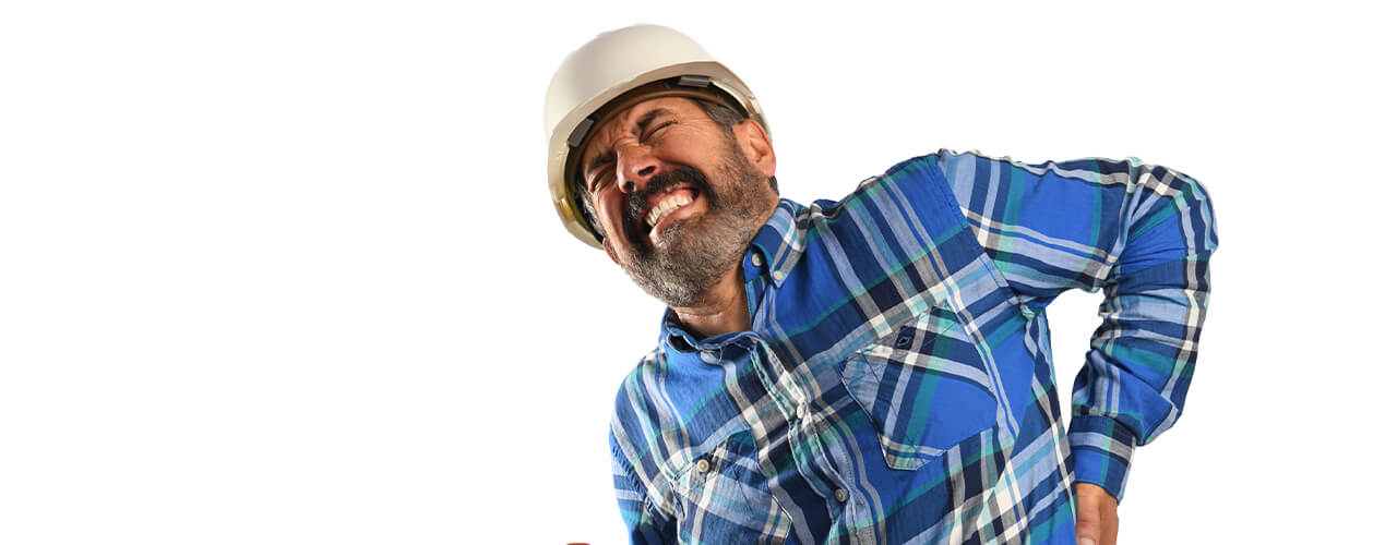 A man with a hard hat leans over with his hand on his lower back, making a face as if he's in pain.
